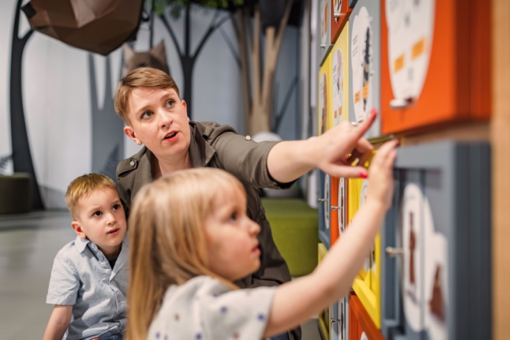 two children interact with a museum exhibit while their teacher supervises